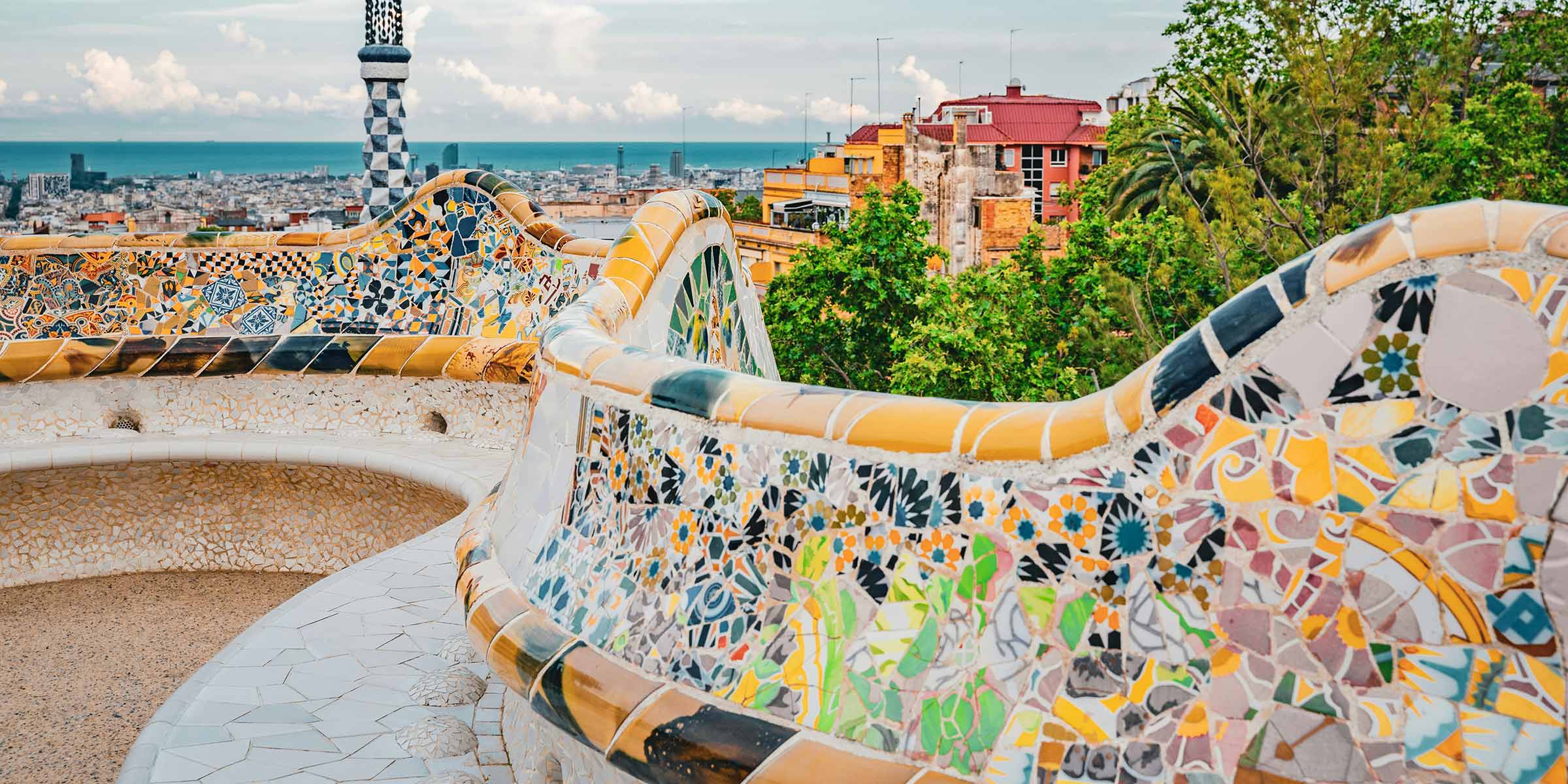 A colorful, curved, mosaic wall in front of the city of Barcelona.