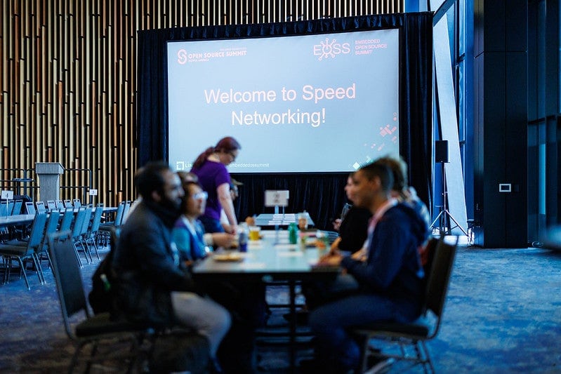 A group of people at a table in front of a screen that reads "Welcome to speed networking".
