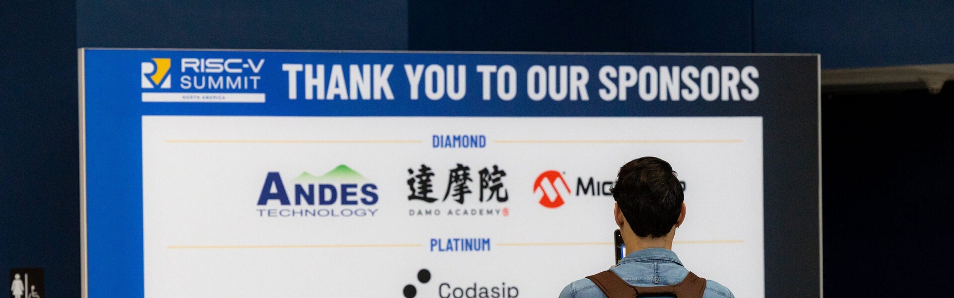 A man looking at a sign of sponsors.